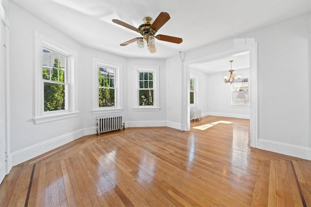 empty room with plenty of natural light, light wood-type flooring, ceiling fan with notable chandelier, and radiator