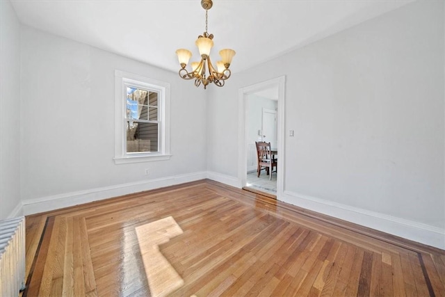 empty room featuring a chandelier, radiator heating unit, and hardwood / wood-style flooring