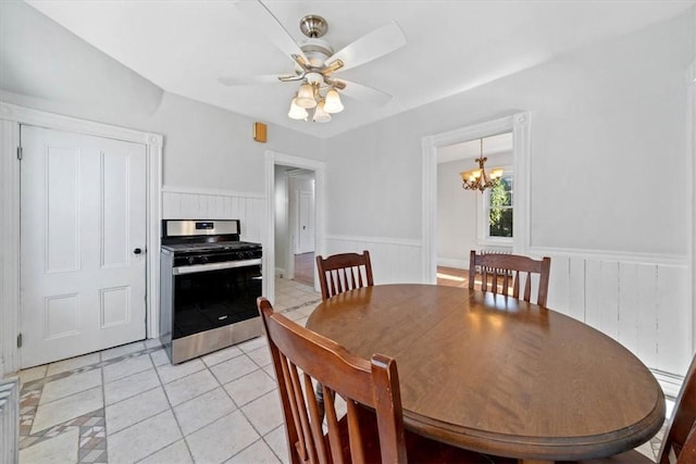 dining area featuring wood walls, light tile patterned flooring, and ceiling fan with notable chandelier