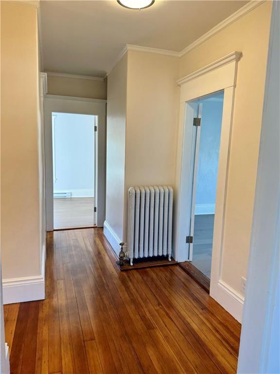 hallway featuring baseboard heating, dark hardwood / wood-style flooring, crown molding, and radiator heating unit