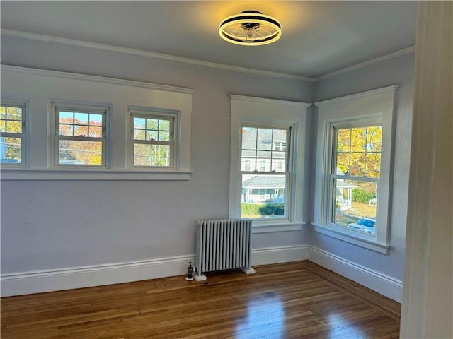 empty room featuring wood-type flooring, radiator heating unit, and ornamental molding