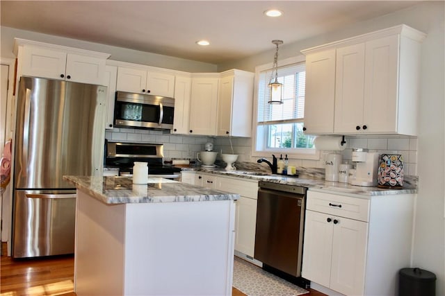 kitchen featuring white cabinetry, appliances with stainless steel finishes, decorative light fixtures, and a kitchen island