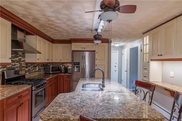 kitchen with a spacious island, wall chimney range hood, sink, light stone countertops, and appliances with stainless steel finishes