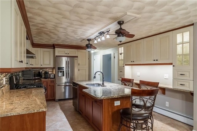 kitchen featuring appliances with stainless steel finishes, ceiling fan, a kitchen island with sink, sink, and a baseboard radiator