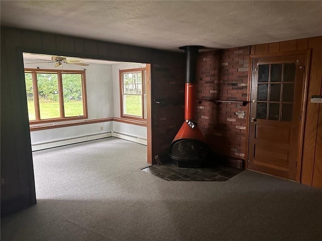 carpeted foyer featuring a wood stove, ceiling fan, a textured ceiling, and a baseboard heating unit