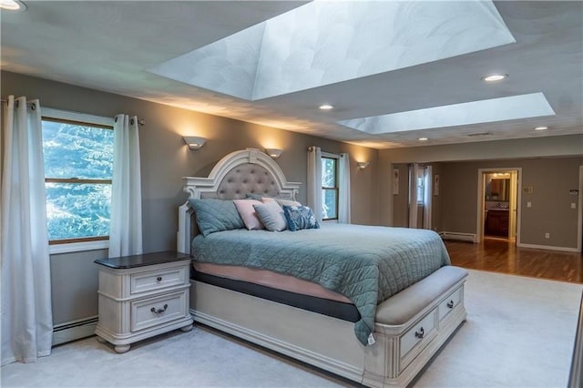 bedroom with light hardwood / wood-style floors, a skylight, a tray ceiling, and a baseboard radiator