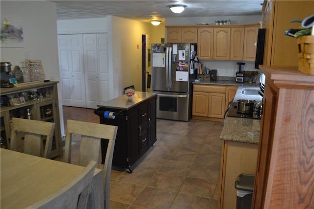 kitchen featuring stainless steel fridge, light stone counters, black range oven, sink, and light brown cabinets