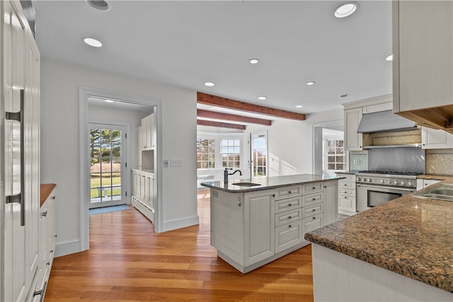 kitchen with light wood-type flooring, ventilation hood, high end stainless steel range oven, beamed ceiling, and white cabinetry