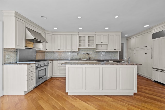 kitchen with a center island with sink, wall chimney range hood, stainless steel range, and light hardwood / wood-style flooring