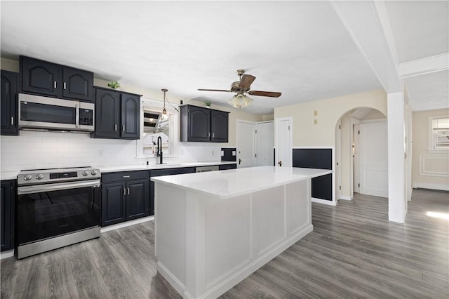 kitchen featuring arched walkways, light countertops, appliances with stainless steel finishes, a sink, and wood finished floors