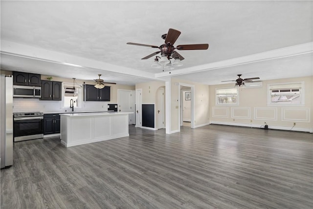 kitchen featuring stainless steel appliances, light countertops, open floor plan, a kitchen island, and a sink