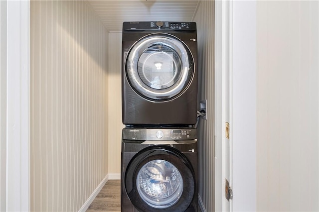 laundry area featuring laundry area, stacked washing maching and dryer, wood finished floors, and baseboards