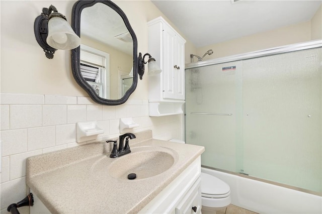 full bath featuring wainscoting, toilet, enclosed tub / shower combo, vanity, and tile walls