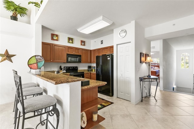 kitchen featuring dark stone counters, black appliances, light tile patterned floors, a kitchen bar, and kitchen peninsula