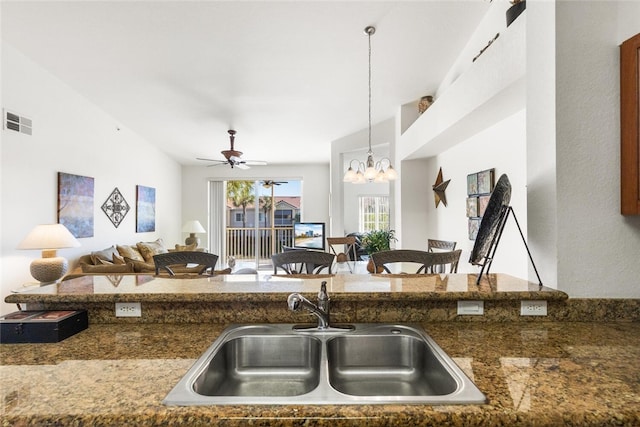 kitchen featuring ceiling fan with notable chandelier, decorative light fixtures, dark stone counters, and sink