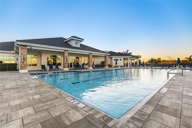 pool at dusk with cooling unit and a patio area