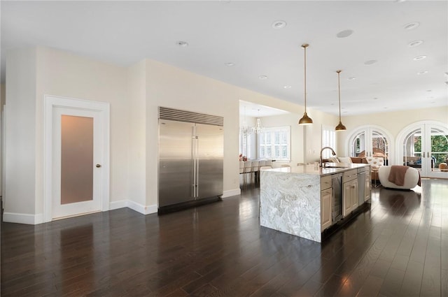 kitchen with light stone countertops, a kitchen island with sink, pendant lighting, stainless steel built in fridge, and wine cooler