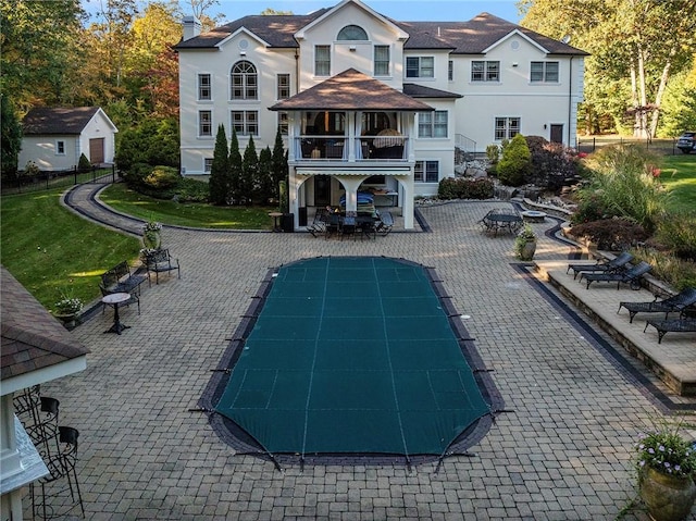 rear view of house featuring a balcony, a patio, and a covered pool