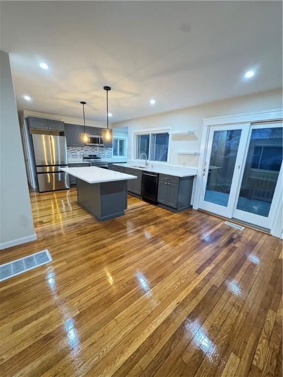 kitchen with decorative light fixtures, a kitchen island, light hardwood / wood-style floors, and stainless steel appliances