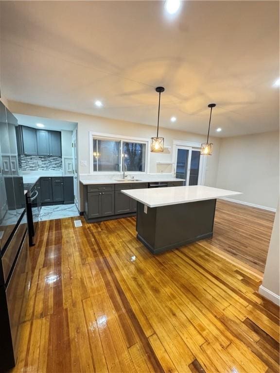 kitchen with sink, backsplash, pendant lighting, a kitchen island, and hardwood / wood-style flooring