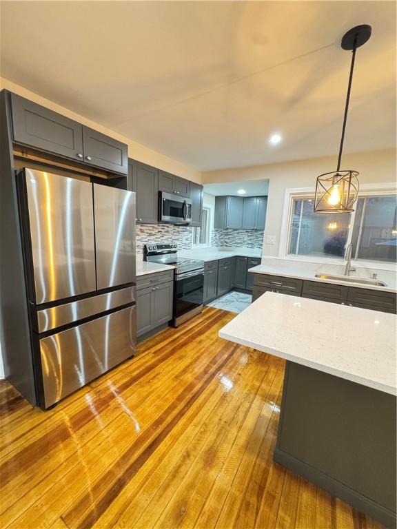 kitchen with sink, stainless steel appliances, tasteful backsplash, light hardwood / wood-style floors, and decorative light fixtures