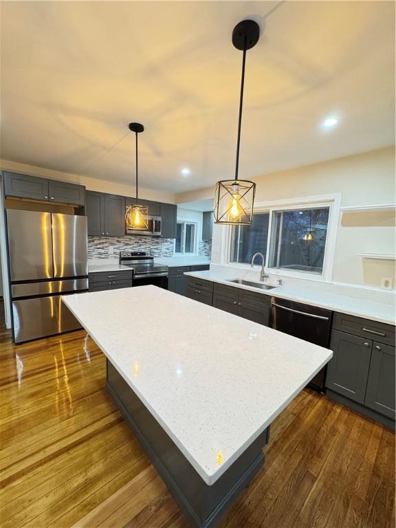 kitchen featuring stainless steel appliances, a kitchen island, hanging light fixtures, and sink