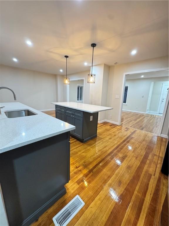 kitchen with sink, light stone counters, light hardwood / wood-style flooring, pendant lighting, and a kitchen island with sink