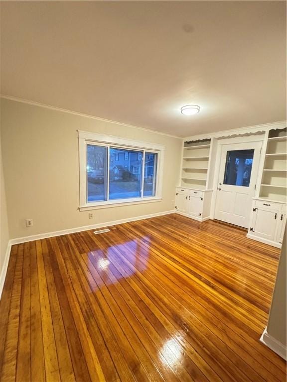 unfurnished living room with built in shelves, crown molding, and light hardwood / wood-style flooring