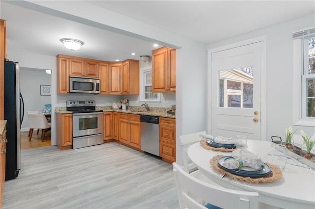 kitchen featuring appliances with stainless steel finishes, light wood-type flooring, light stone counters, and sink