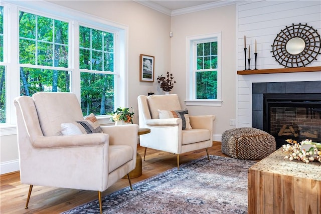 living area featuring a tile fireplace, crown molding, a healthy amount of sunlight, and wood-type flooring