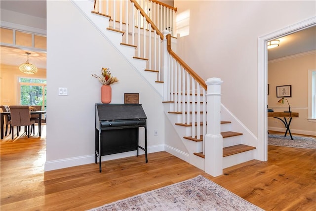 stairway with wood-type flooring, ornamental molding, and a notable chandelier