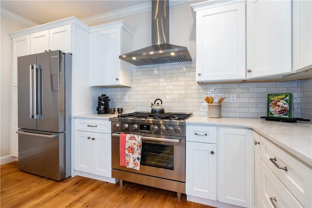 kitchen with ornamental molding, wall chimney exhaust hood, high end appliances, white cabinets, and light hardwood / wood-style floors