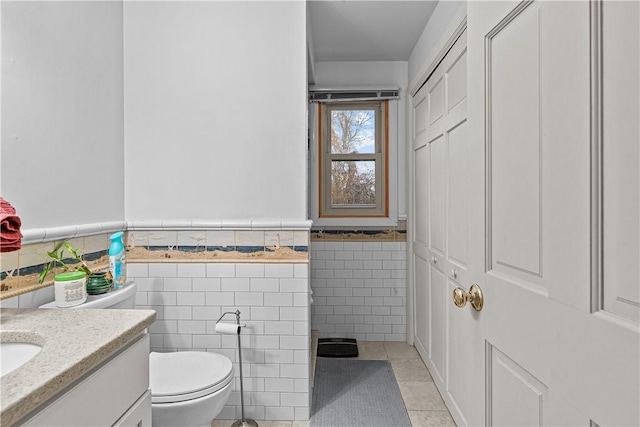 bathroom with tile patterned flooring, vanity, toilet, and tile walls