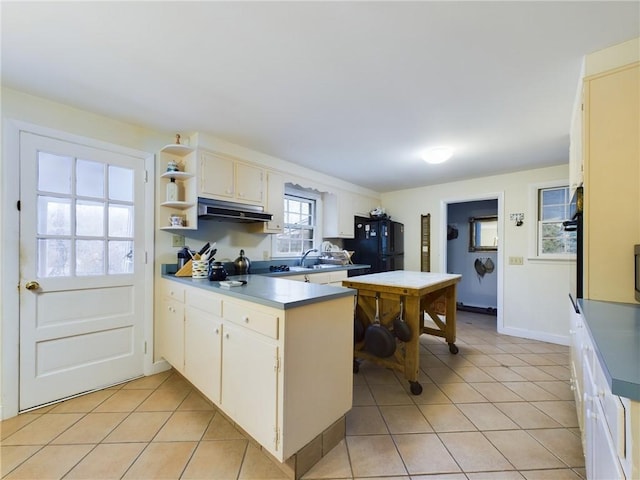 kitchen with kitchen peninsula, sink, black fridge, and light tile patterned flooring