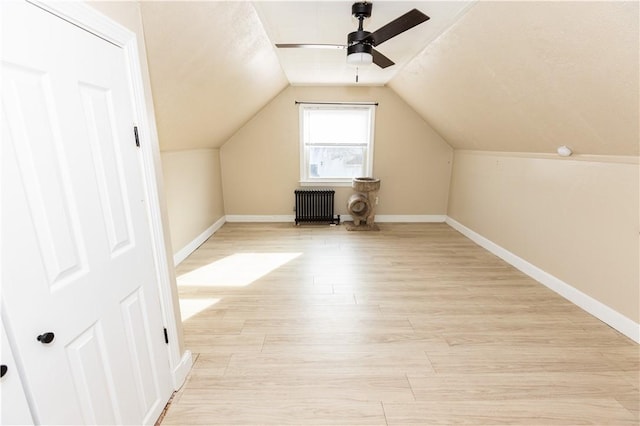 additional living space with radiator heating unit, light hardwood / wood-style flooring, vaulted ceiling, and ceiling fan