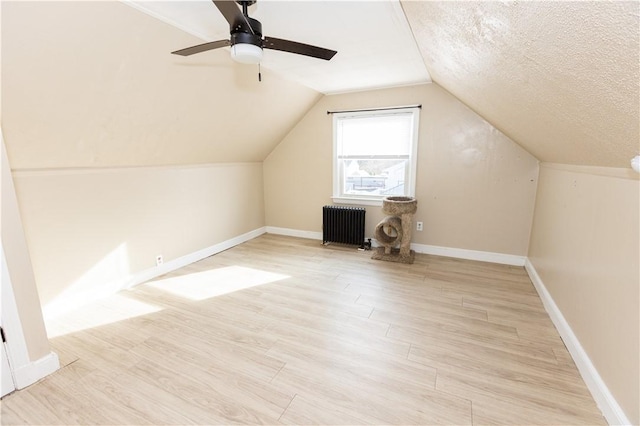 additional living space with ceiling fan, radiator heating unit, light hardwood / wood-style flooring, a textured ceiling, and lofted ceiling