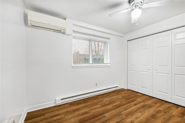 unfurnished bedroom featuring ceiling fan, a baseboard heating unit, a wall unit AC, a textured ceiling, and hardwood / wood-style flooring