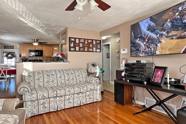 living room with a textured ceiling, light wood-type flooring, and ceiling fan