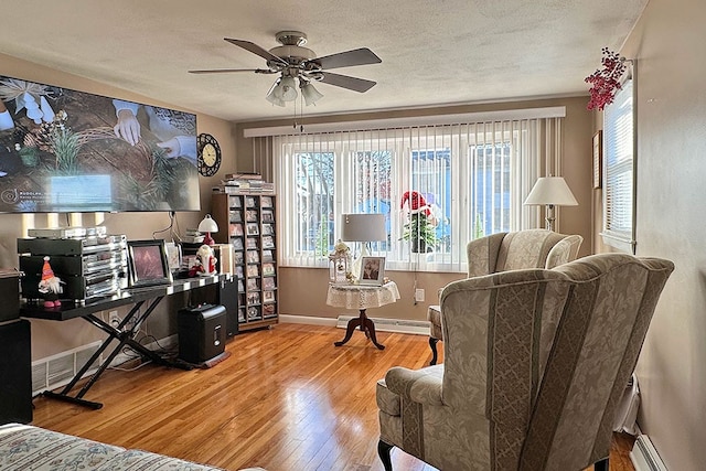 living area with wood-type flooring, a textured ceiling, baseboard heating, and ceiling fan