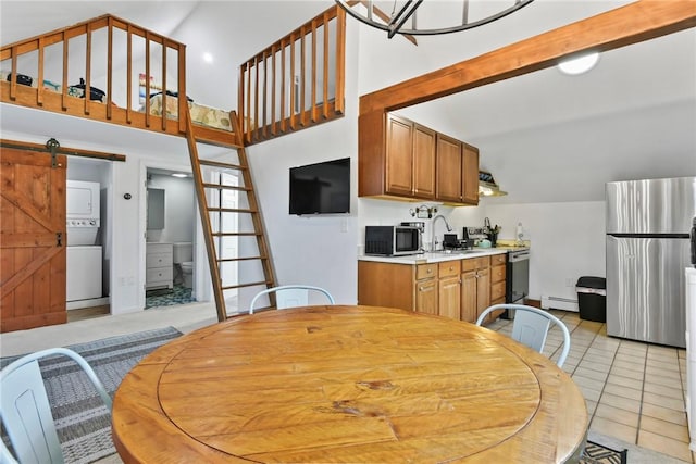 kitchen with sink, a barn door, stacked washing maching and dryer, baseboard heating, and appliances with stainless steel finishes