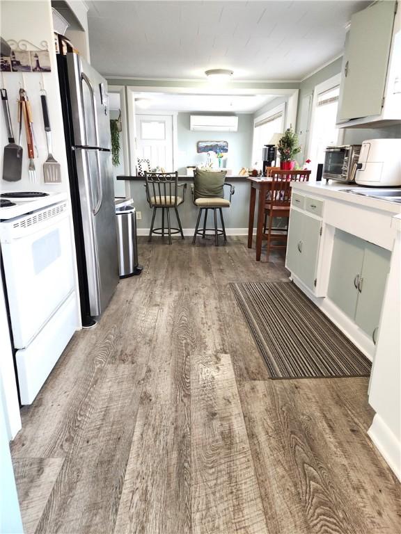 kitchen featuring stainless steel refrigerator, white cabinetry, a wall mounted air conditioner, white electric range, and light hardwood / wood-style floors