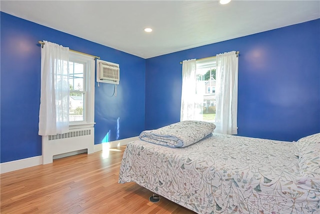 bedroom featuring hardwood / wood-style floors, radiator, and a wall mounted AC