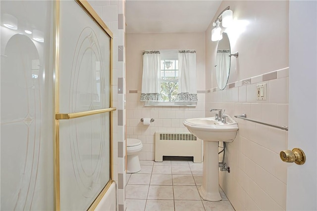 bathroom featuring radiator heating unit, bath / shower combo with glass door, tile walls, and tile patterned flooring