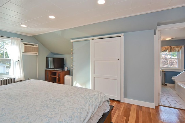 bedroom featuring lofted ceiling, light wood-type flooring, an AC wall unit, and multiple windows