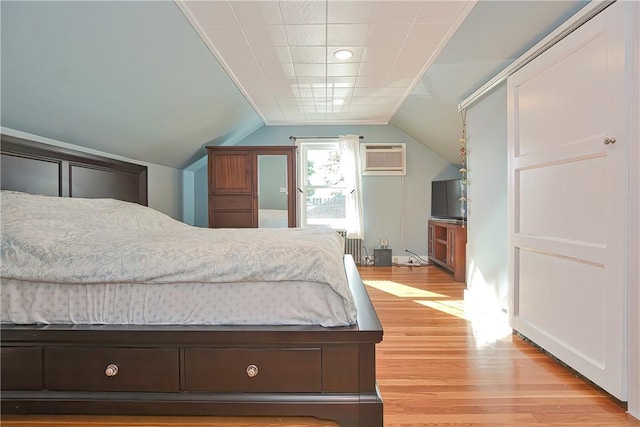 bedroom featuring light hardwood / wood-style flooring, lofted ceiling, and a wall unit AC