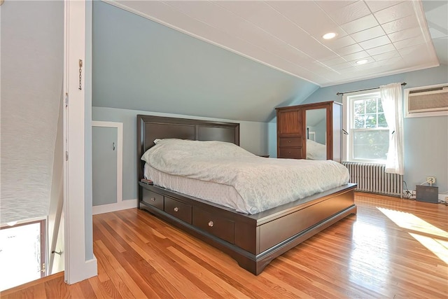 bedroom with a wall unit AC, radiator, light hardwood / wood-style flooring, and vaulted ceiling