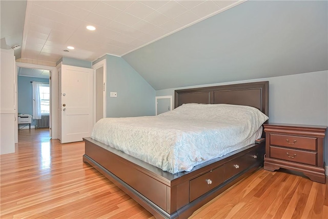 bedroom featuring radiator heating unit, light hardwood / wood-style flooring, and lofted ceiling