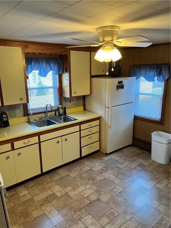 kitchen with ceiling fan, white refrigerator, sink, and wooden walls