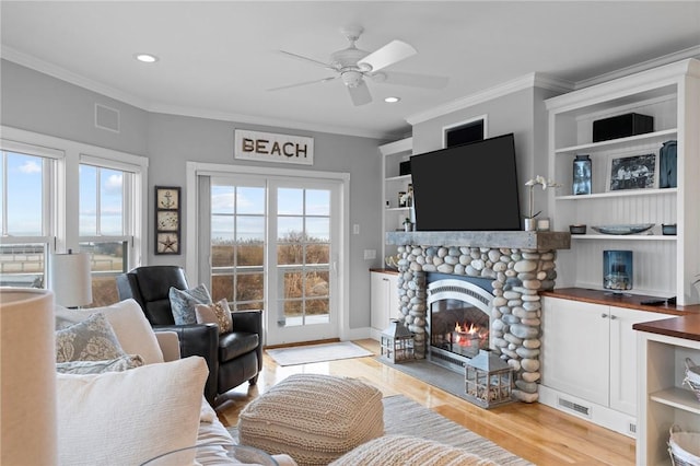 living room with crown molding, light hardwood / wood-style flooring, a healthy amount of sunlight, and a stone fireplace