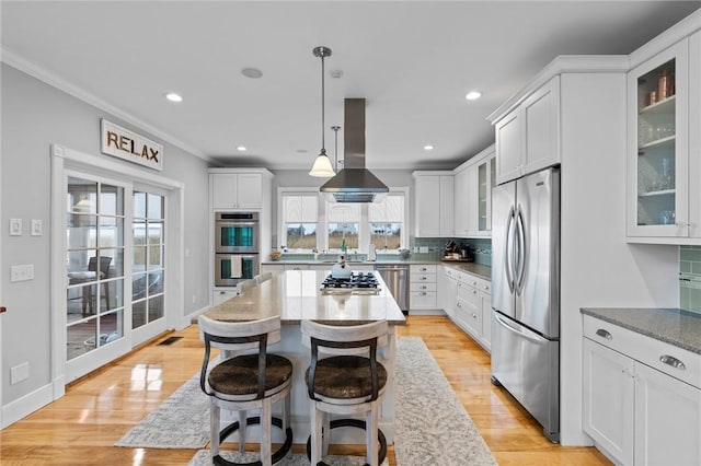 kitchen with stainless steel appliances, white cabinetry, hanging light fixtures, and island range hood